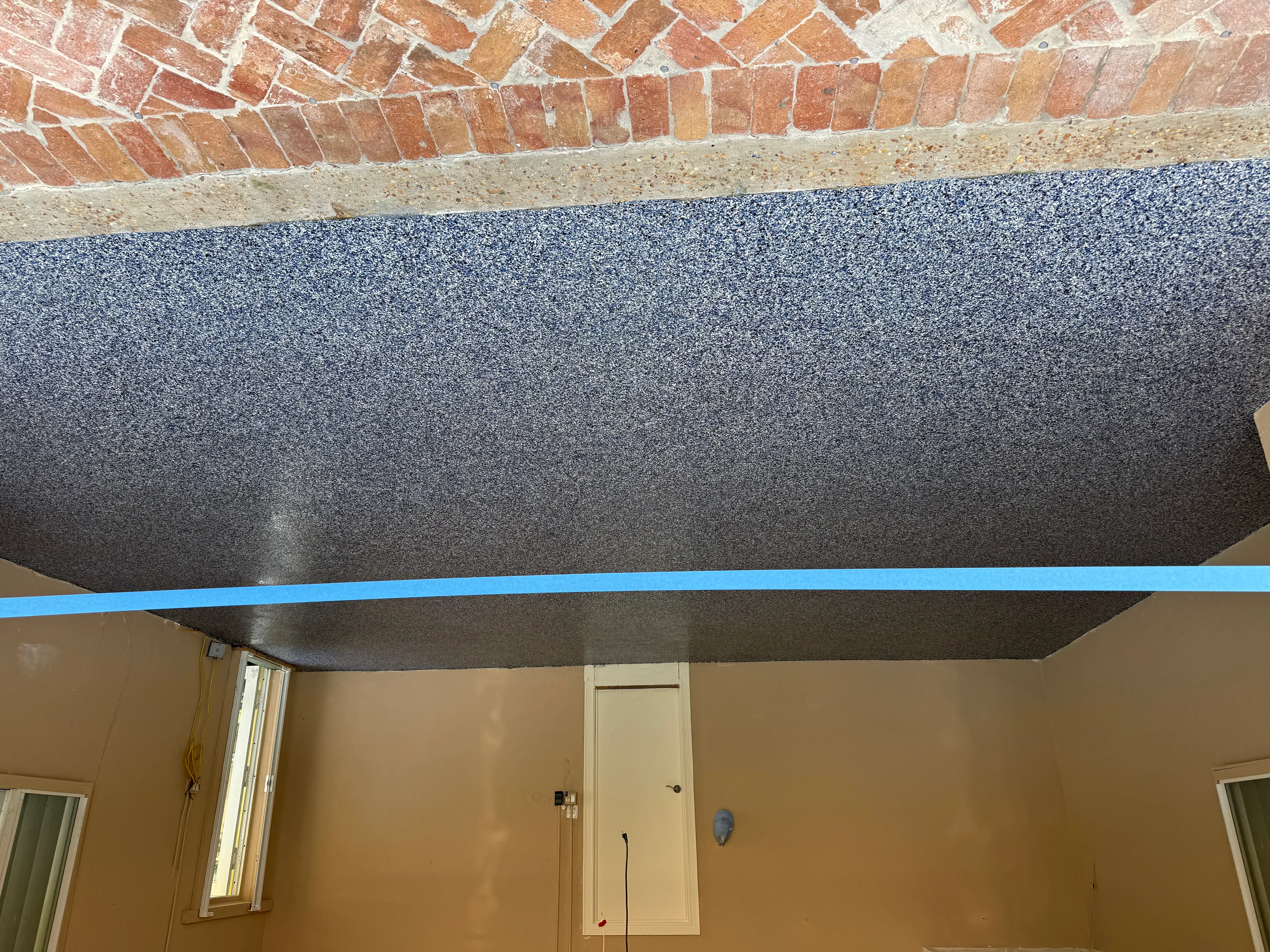 Finished concrete ceiling panel with blue trim line below exposed brick and sand base layer