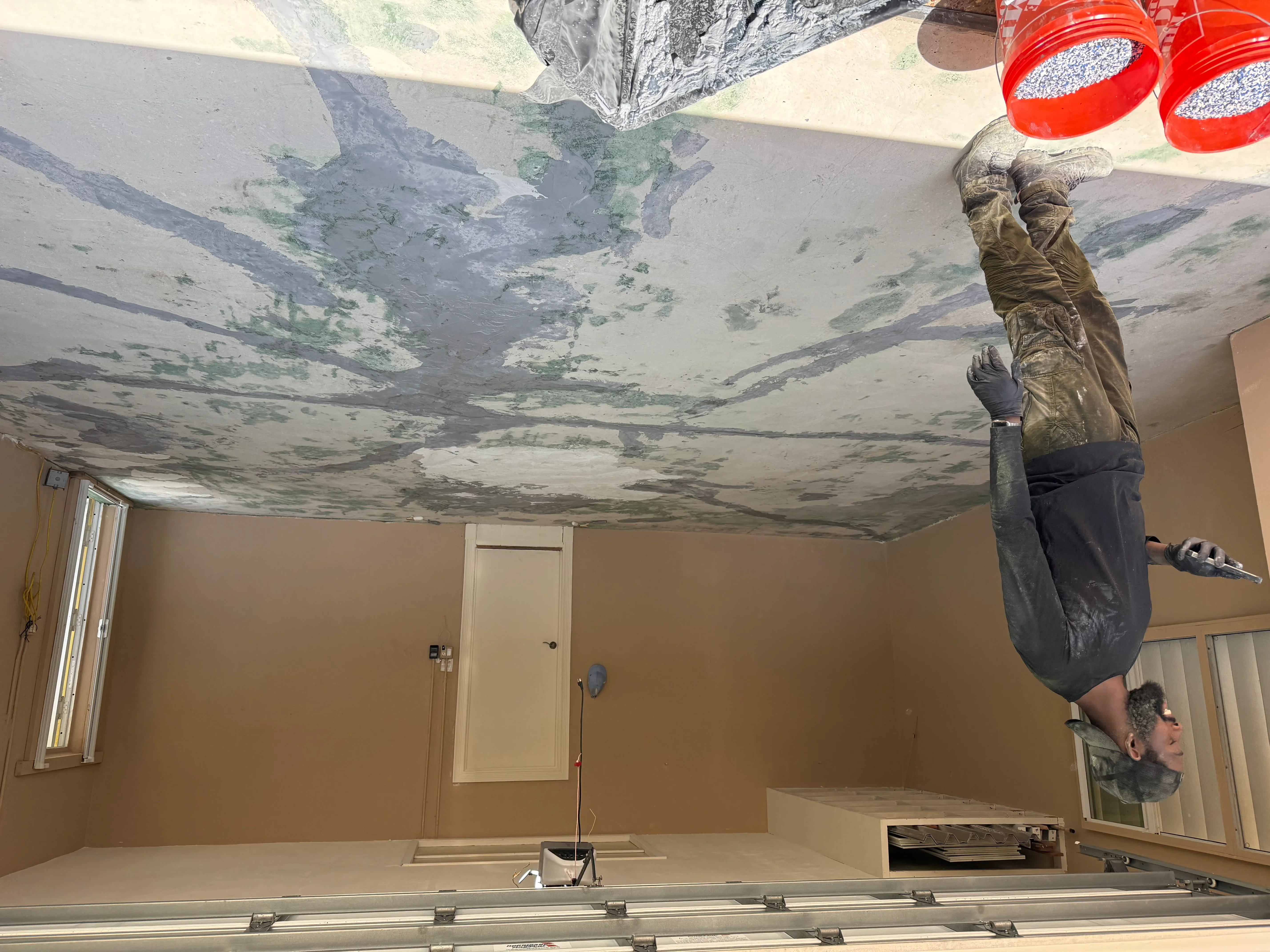 Worker removing damaged drywall from water-stained ceiling with mold growth and discoloration